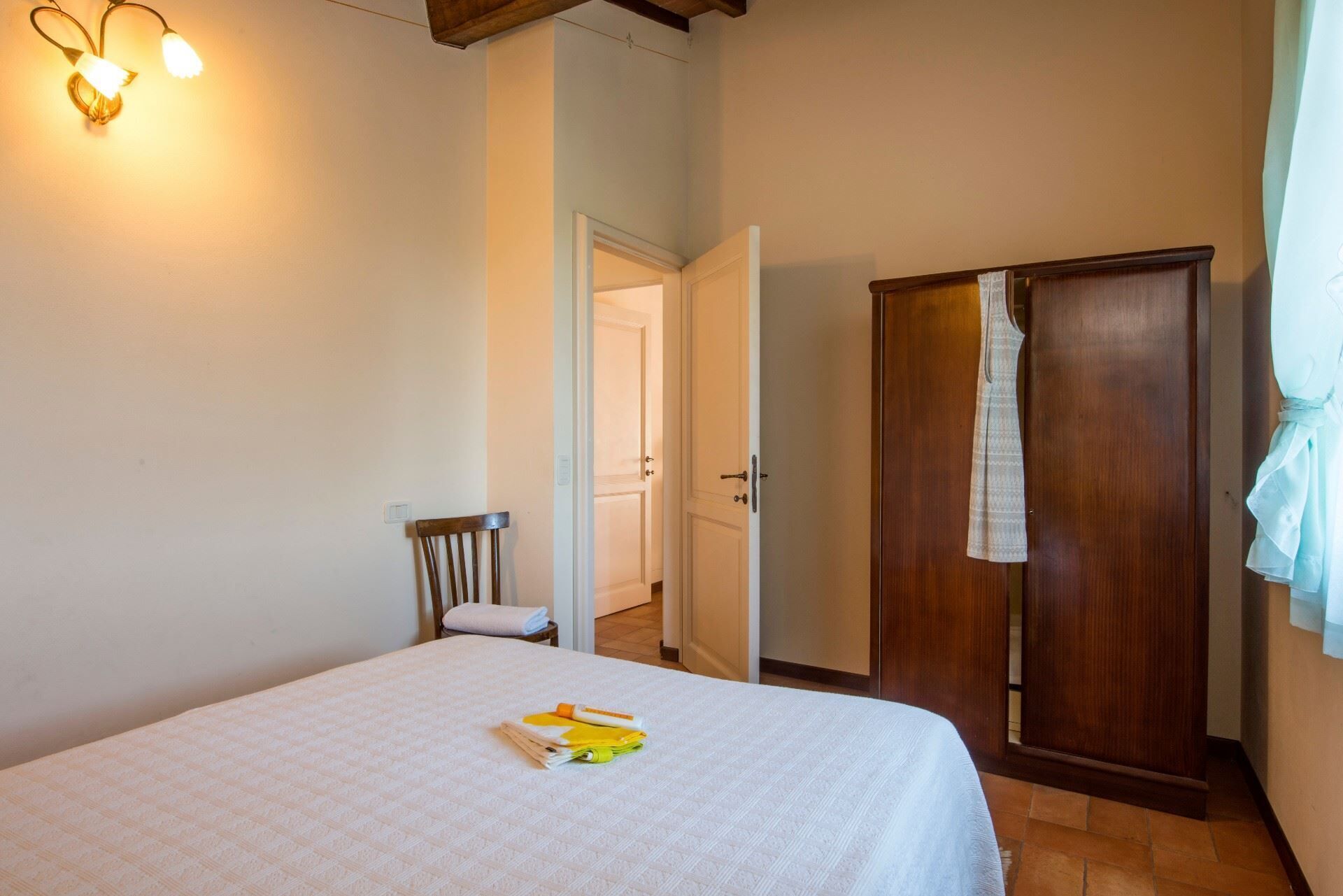 Un dormitorio con cama, armario de madera, una silla e iluminación instalada en la pared.
