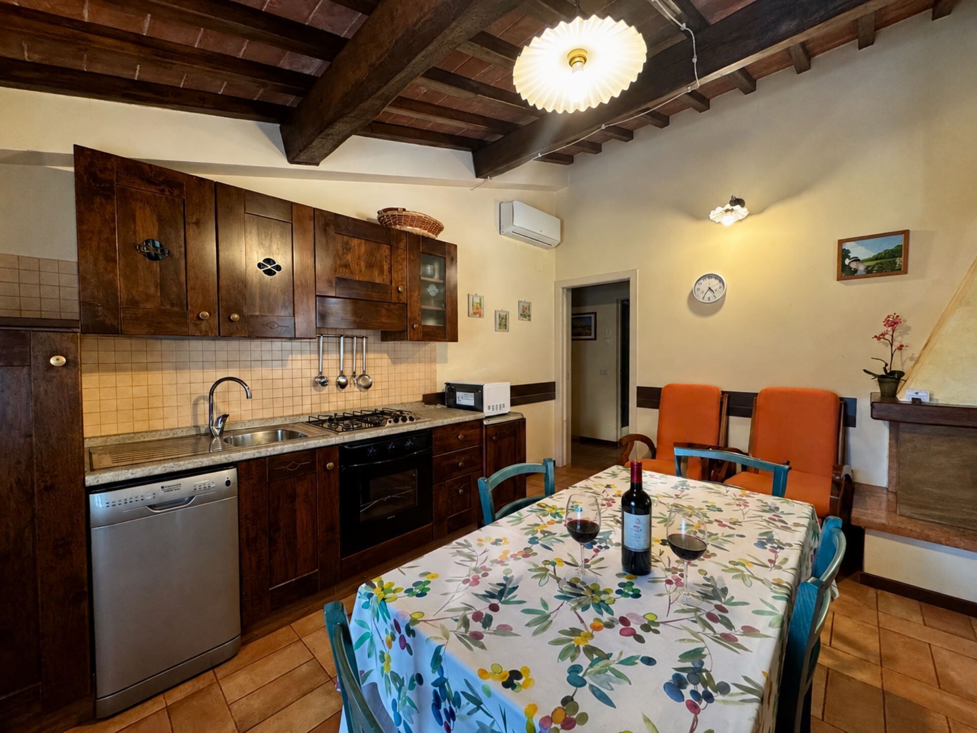 Una cucina con mobili in legno, lavastoviglie e zona pranzo con tavolo apparecchiato per due.
