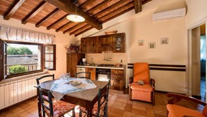 A cozy kitchen with wooden cabinets, a dining table set for four, and a view of the outside through a window. - Agriturismo Case Graziani - Frantoio 3 (Citta della Pieve)