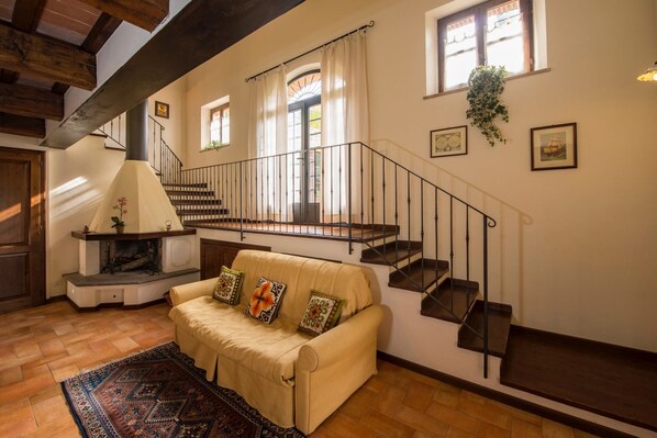 A cozy living room with a sofa, a fireplace, a staircase, and a view of the outside.