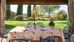 Un'area pranzo all'aperto con un tavolo apparecchiato per quattro persone, circondato da sedie, sotto un pergolato di legno.