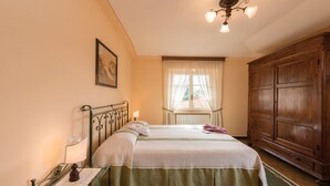 A bedroom with a bed, a nightstand, a wooden wardrobe, a window with curtains, and a ceiling light fixture. - Agriturismo Case Graziani - Palazzo 2 (Citta della Pieve)