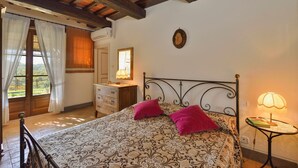 Une chambre à coucher avec un lit, une commode, une table de chevet, une lampe et une fenêtre avec des rideaux.