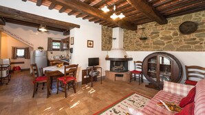 Un salon chaleureux avec une chemin ée, des poutres en bois, des murs en pierre et un coin repas comprenant une table et des chaises.