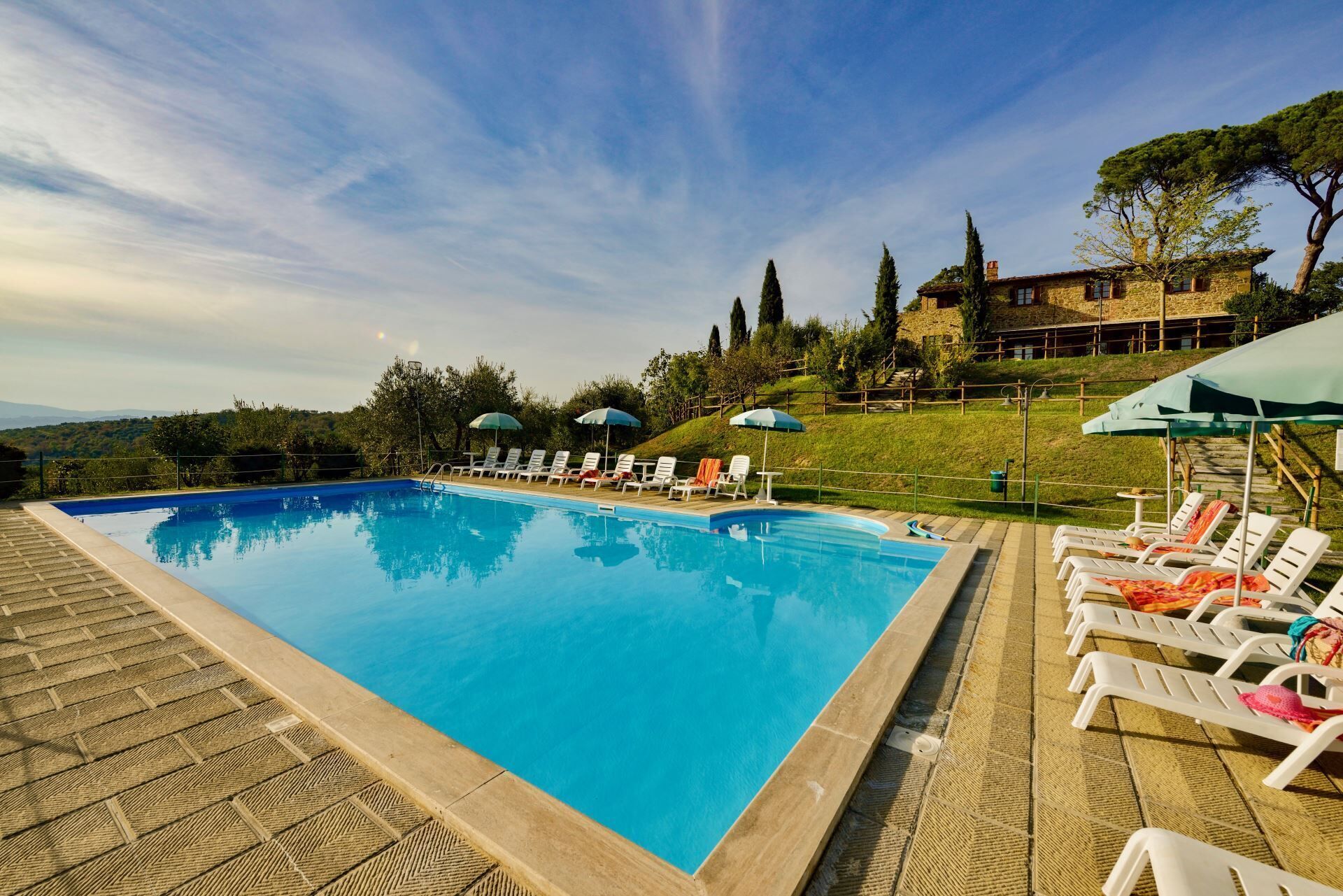 Una piscina con lettini e ombrelloni, circondata da un edificio in pietra e alberi.