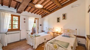 A bedroom with two beds, wooden beams on the ceiling, a radiator, and a window with curtains.