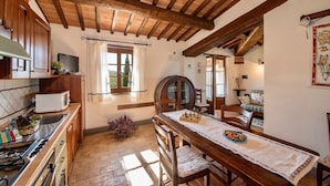 A rustic kitchen with wooden beams, a dining table with chairs, and a window with curtains.