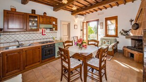 A rustic kitchen with wooden cabinets, a gas stove, and a dining area with a table and chairs. - Agriturismo Malagronda - Quercia (Citta della Pieve)