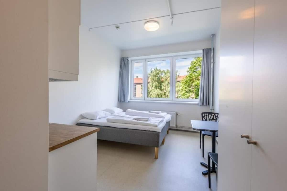 Una habitación pequeña y moderna con cama, una mesa y una ventana con cortinas.