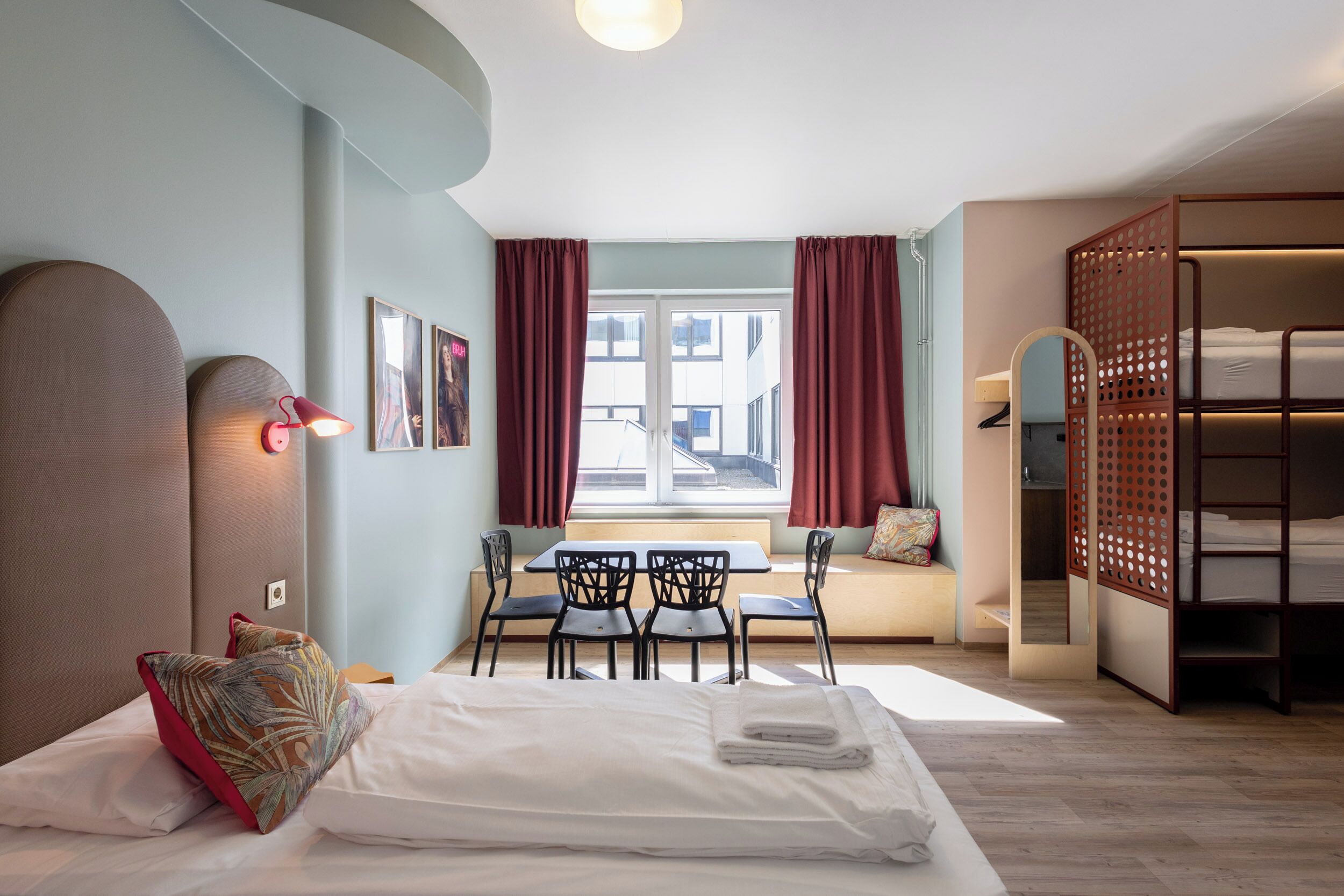 Habitación de hotel con cama, un escritorio con sillas, una ventana con cortinas y una litera.
