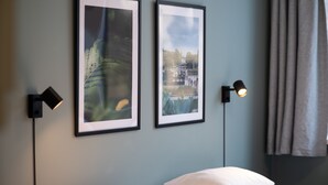 A bedroom with a bed, two framed pictures on the wall, and two wall-mounted lamps.