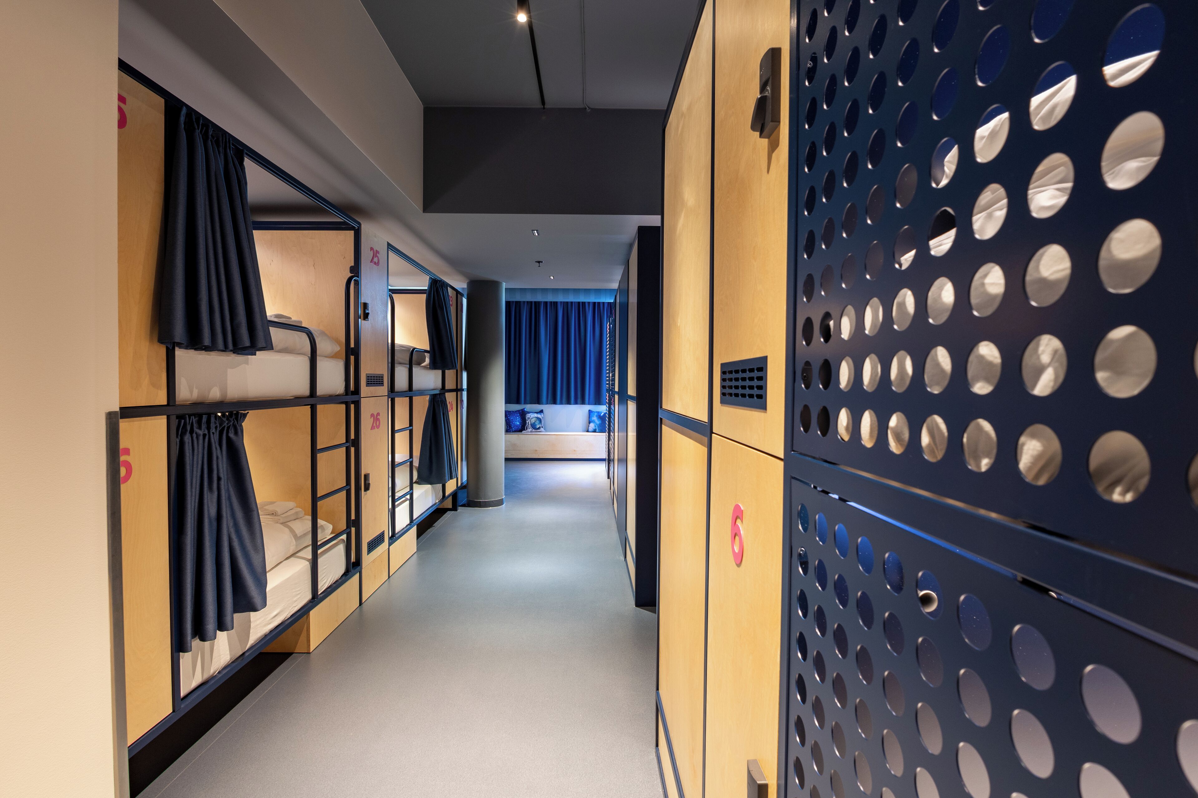 Ein Hotelkorridor mit Stockbetten, einem blauen Vorhang und einer Lochwand.
