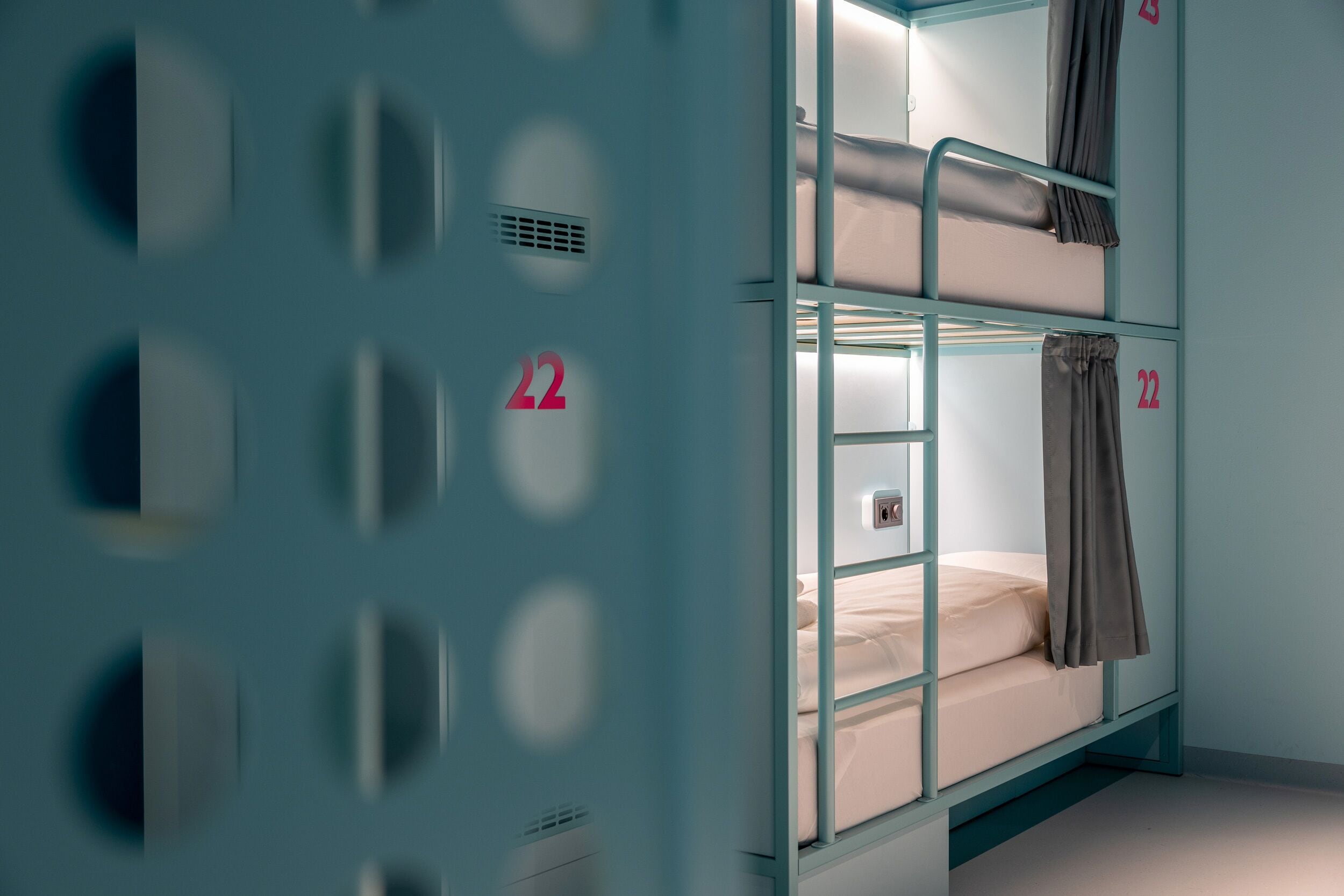 A bunk bed with a number '22' on the wall, a window, and a ventilation grille.
