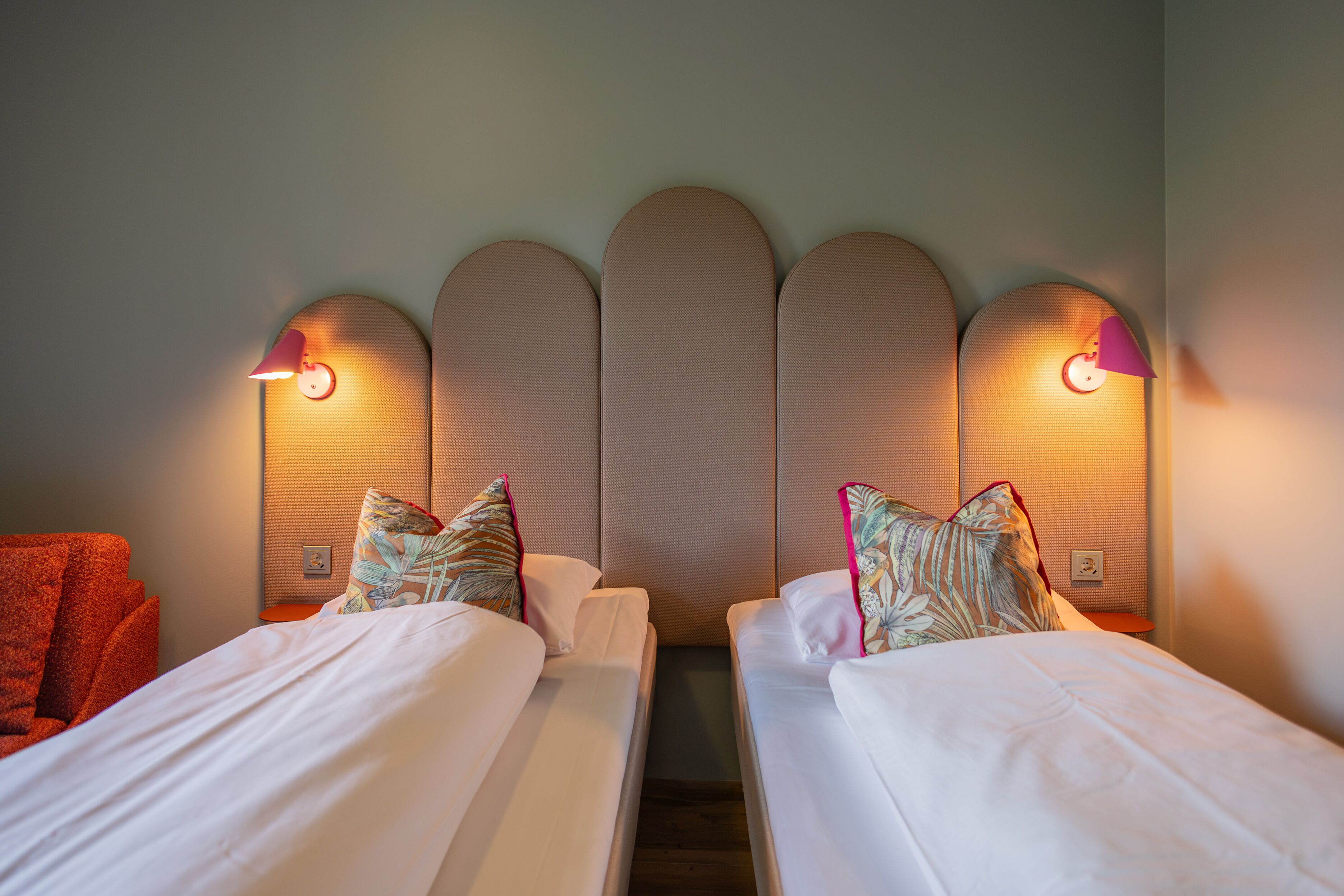 Habitación de hotel con dos camas, cabecero de diseño único y lámparas fijadas a la pared.