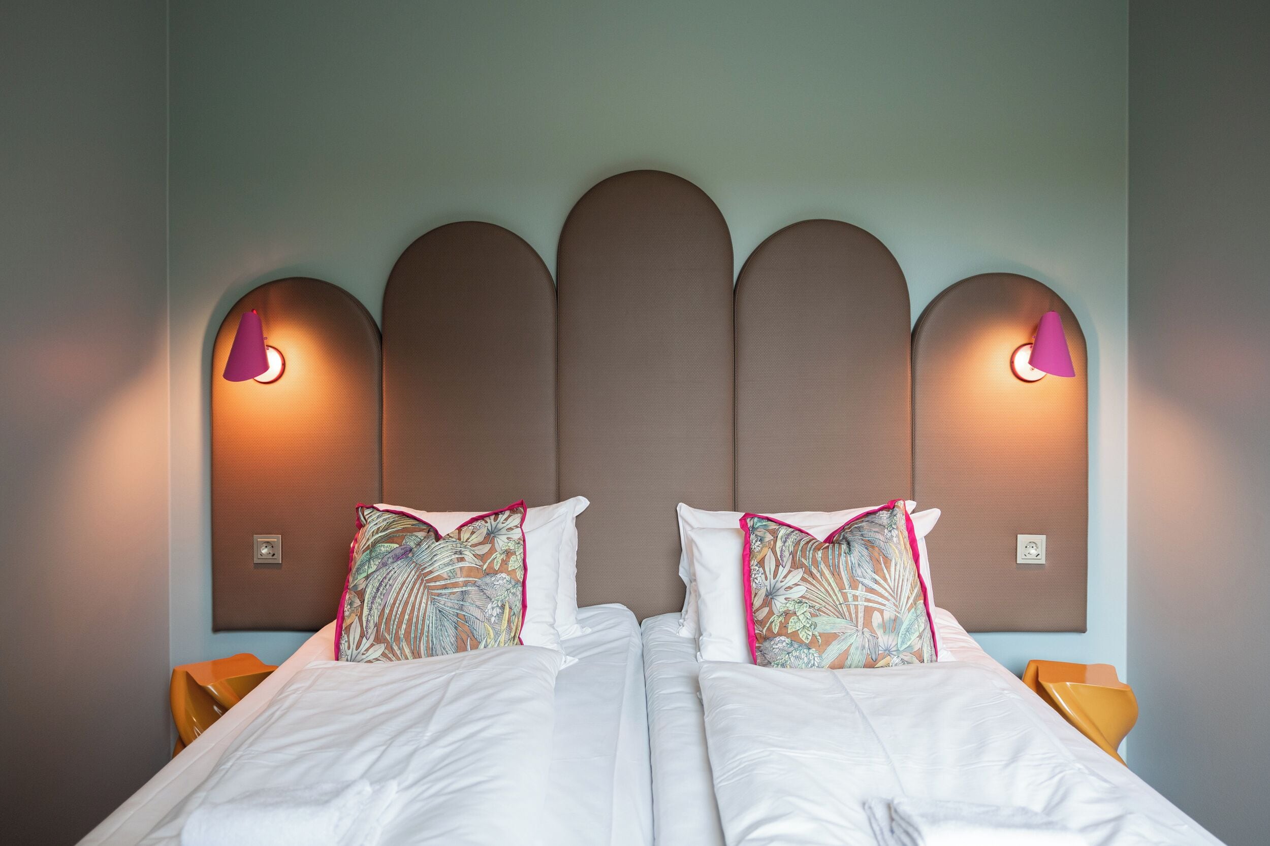 Ein Doppelbett mit weißen Laken, zwei Zierkissen und ein Kopfteil mit individuellem Design, sowie Wandleuchten.