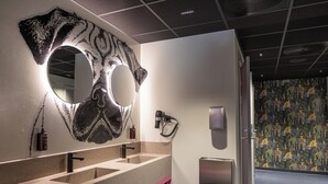 A modern bathroom with a large mirror, two sinks, a hairdryer, and a towel rack.