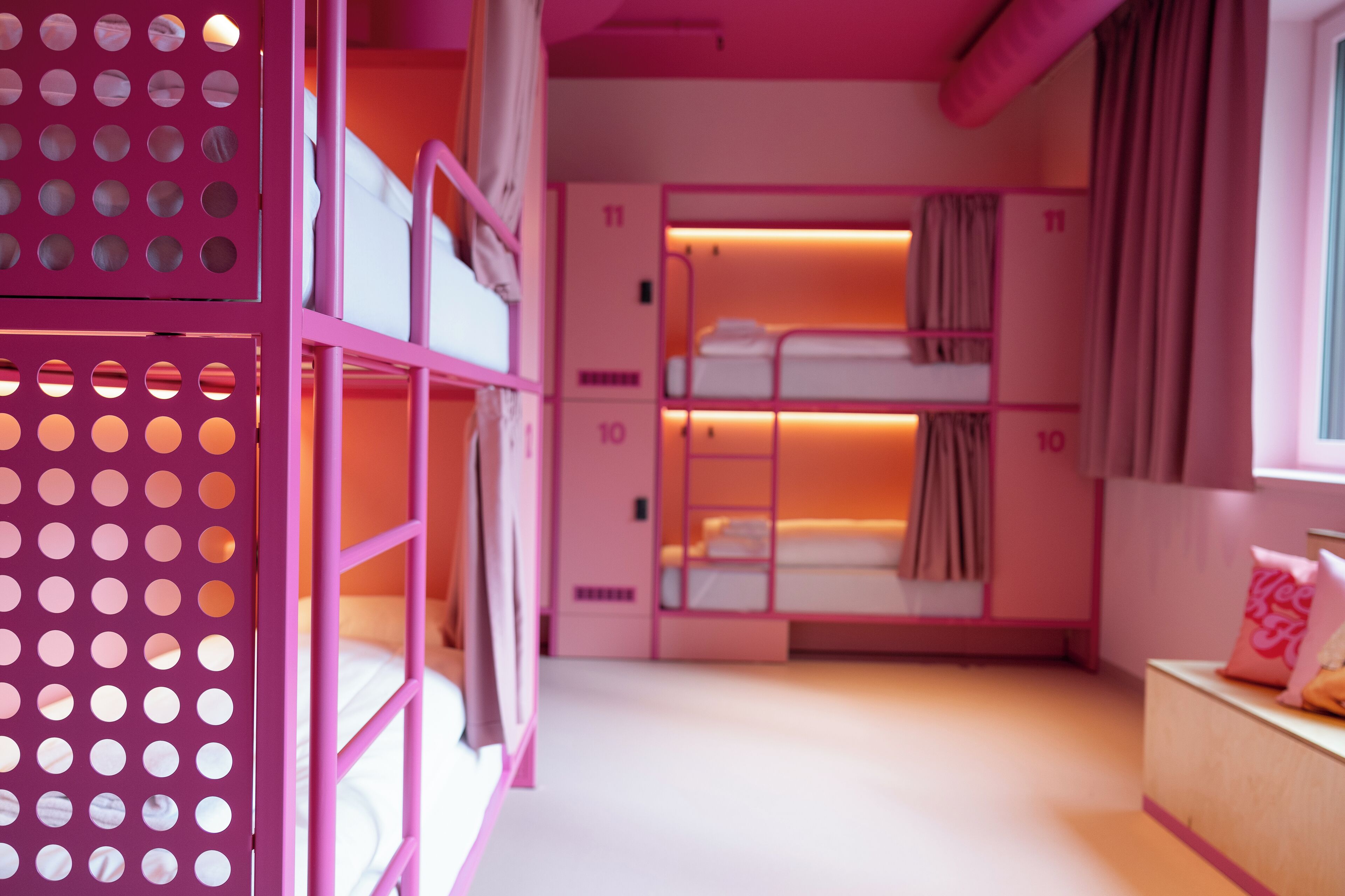 Una habitación con decoración rosa, con literas, un escritorio de madera y una ventana con cortinas.