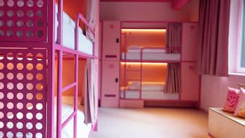 Una habitación con decoración rosa, con literas, un escritorio de madera y una ventana con cortinas.