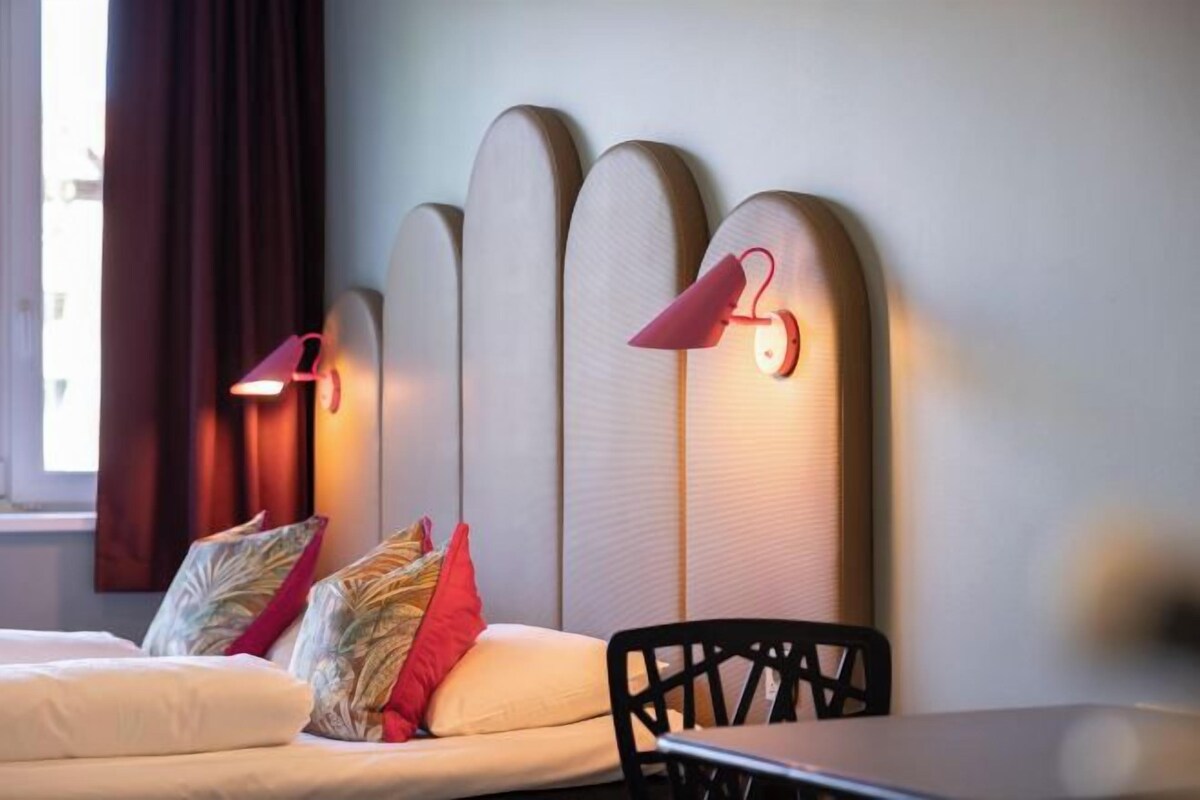 A room with a sofa, pillows, a table, and wall-mounted lamps.