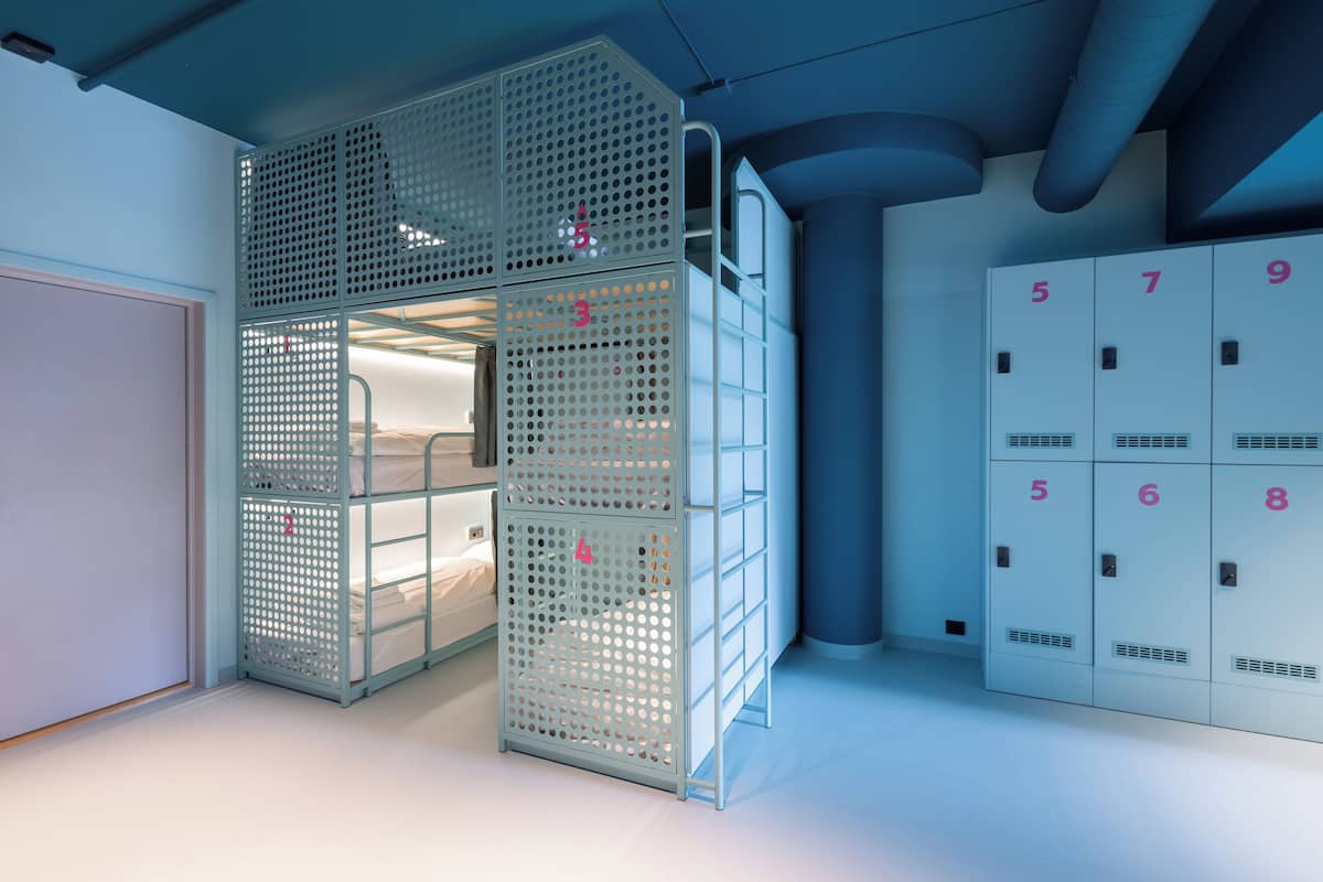 Una habitación de hotel moderna con literas, un armario con taquillas numeradas y un pilar grande.