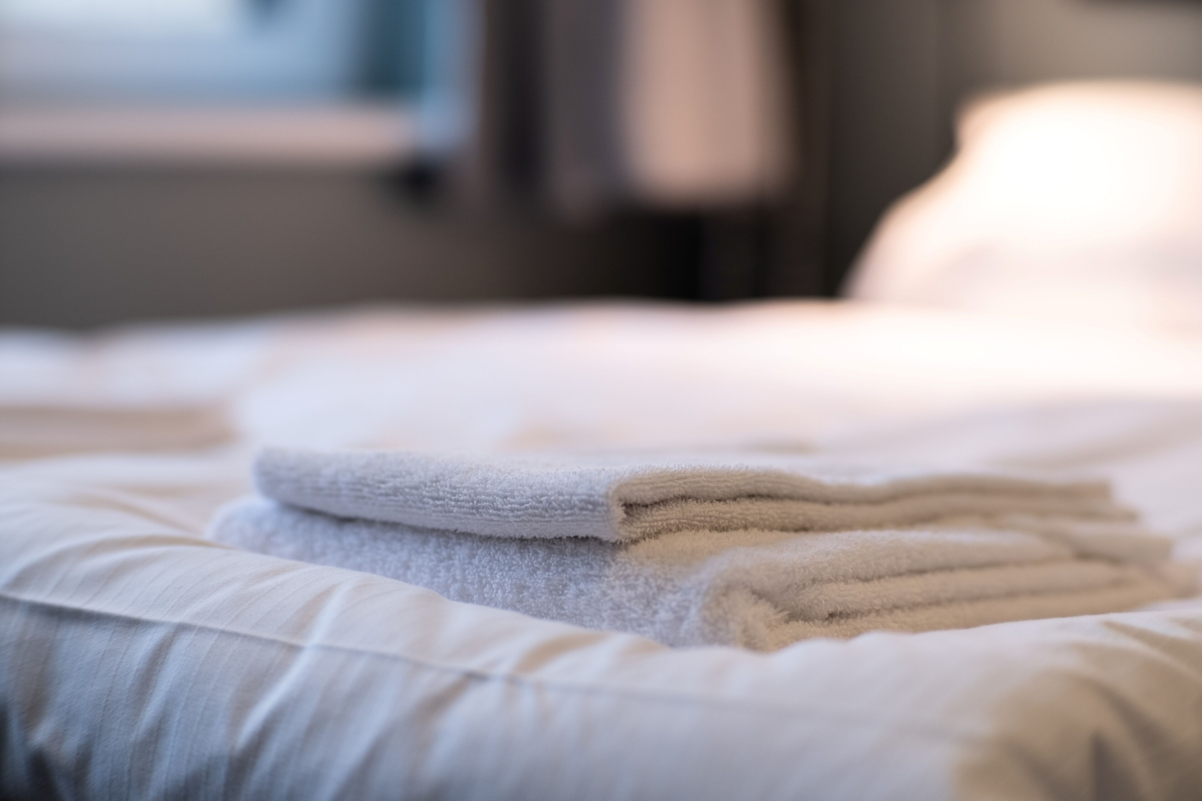 Une serviette blanche, soigneusement pliée, est posée sur un lit, à côté d’un oreiller.