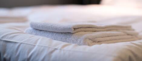 Une serviette blanche, soigneusement pliée, est posée sur un lit, à côté d’un oreiller.