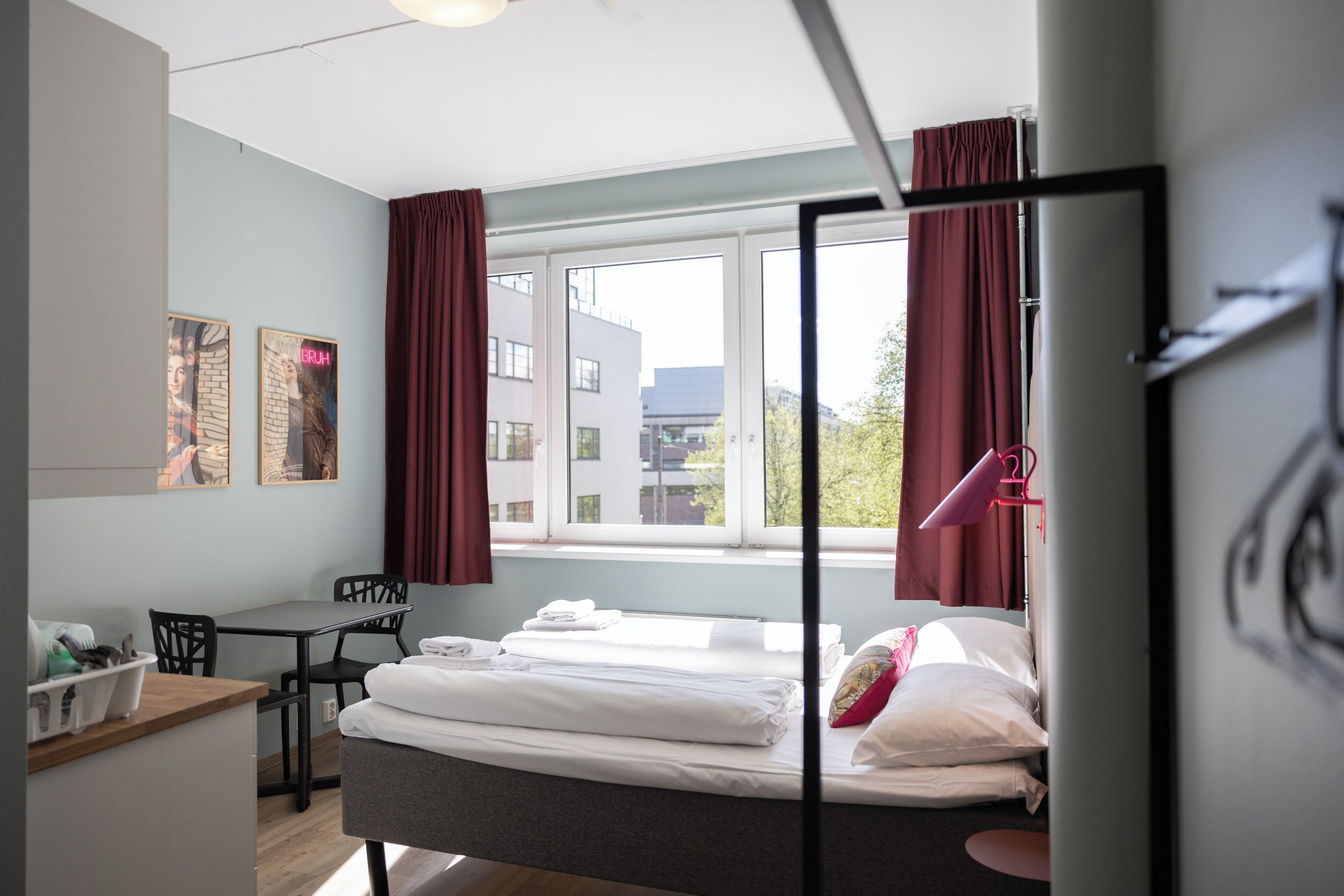A hotel room with a bed, a desk, chairs, and a window with curtains.