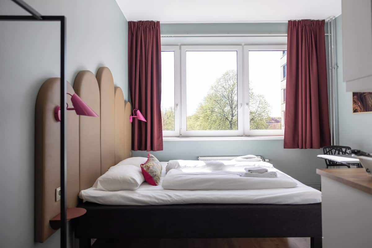 Una habitación de hotel con una cama, una ventana con cortinas, un escritorio y una silla.
