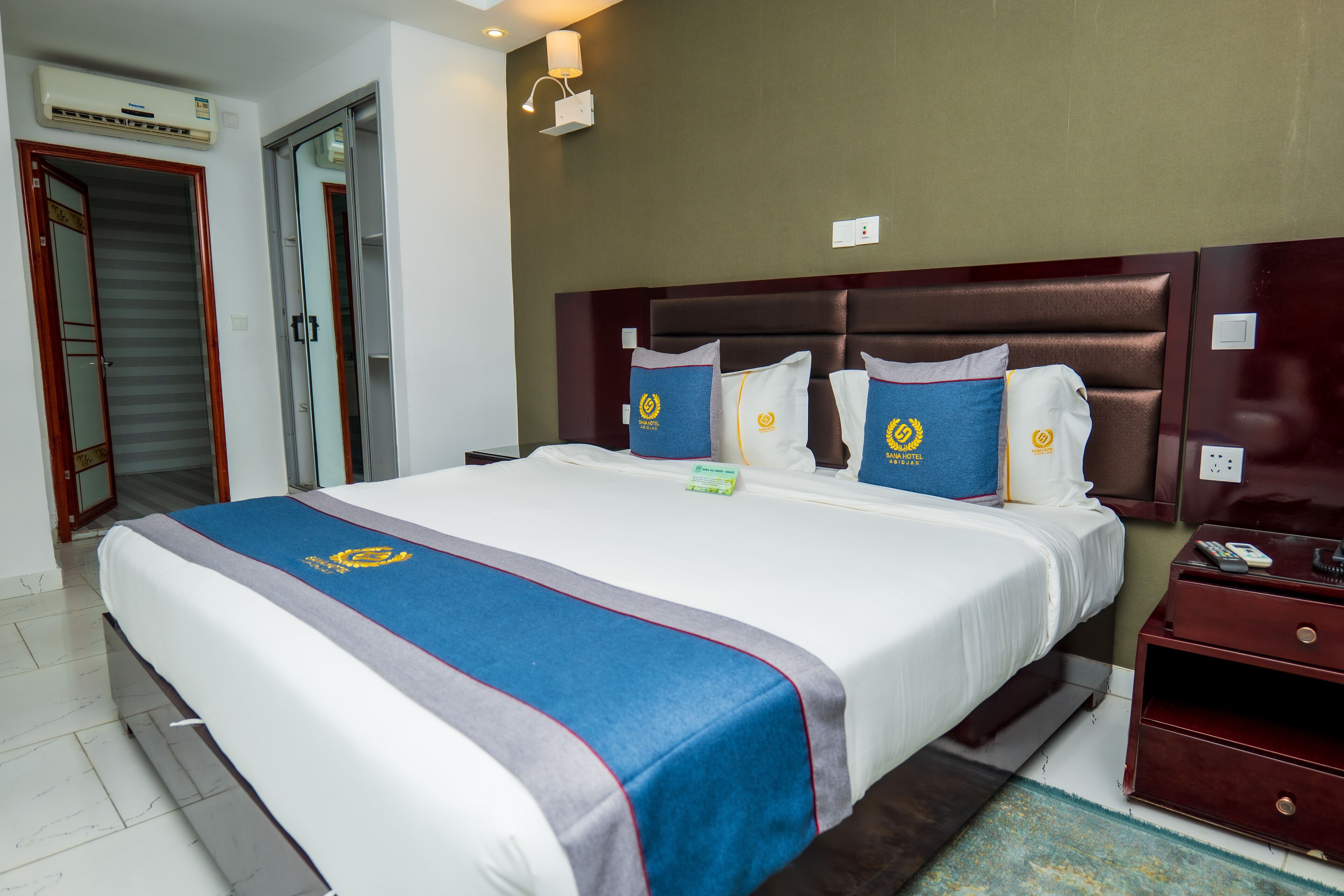 A hotel room with a large bed, a wooden headboard, and a nightstand with a remote control.