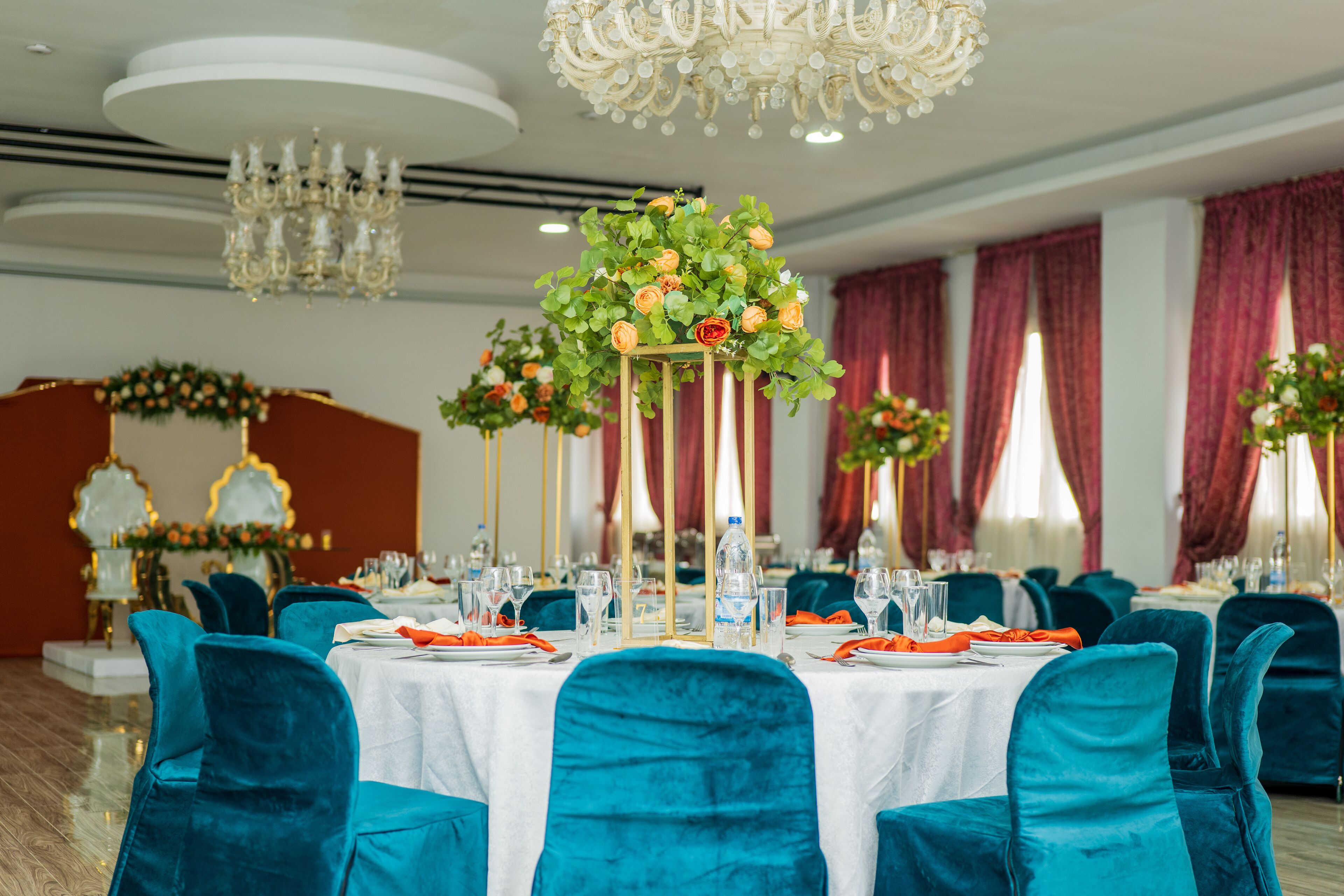 A banquet hall with round tables, teal chairs, and floral centerpieces.