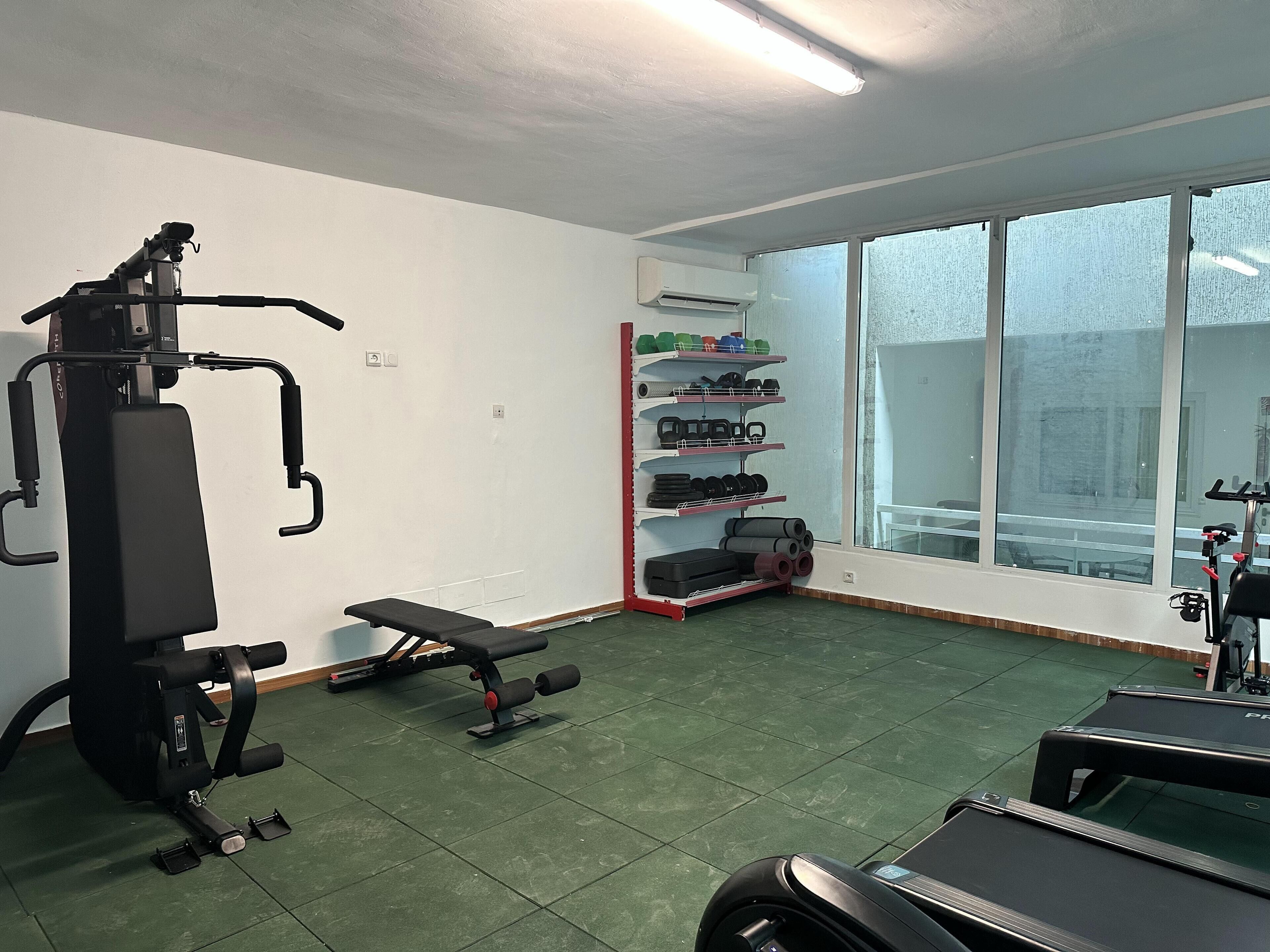 Une salle de sport équipée de machines d’exercice, d’un banc et d’une pile de poids.