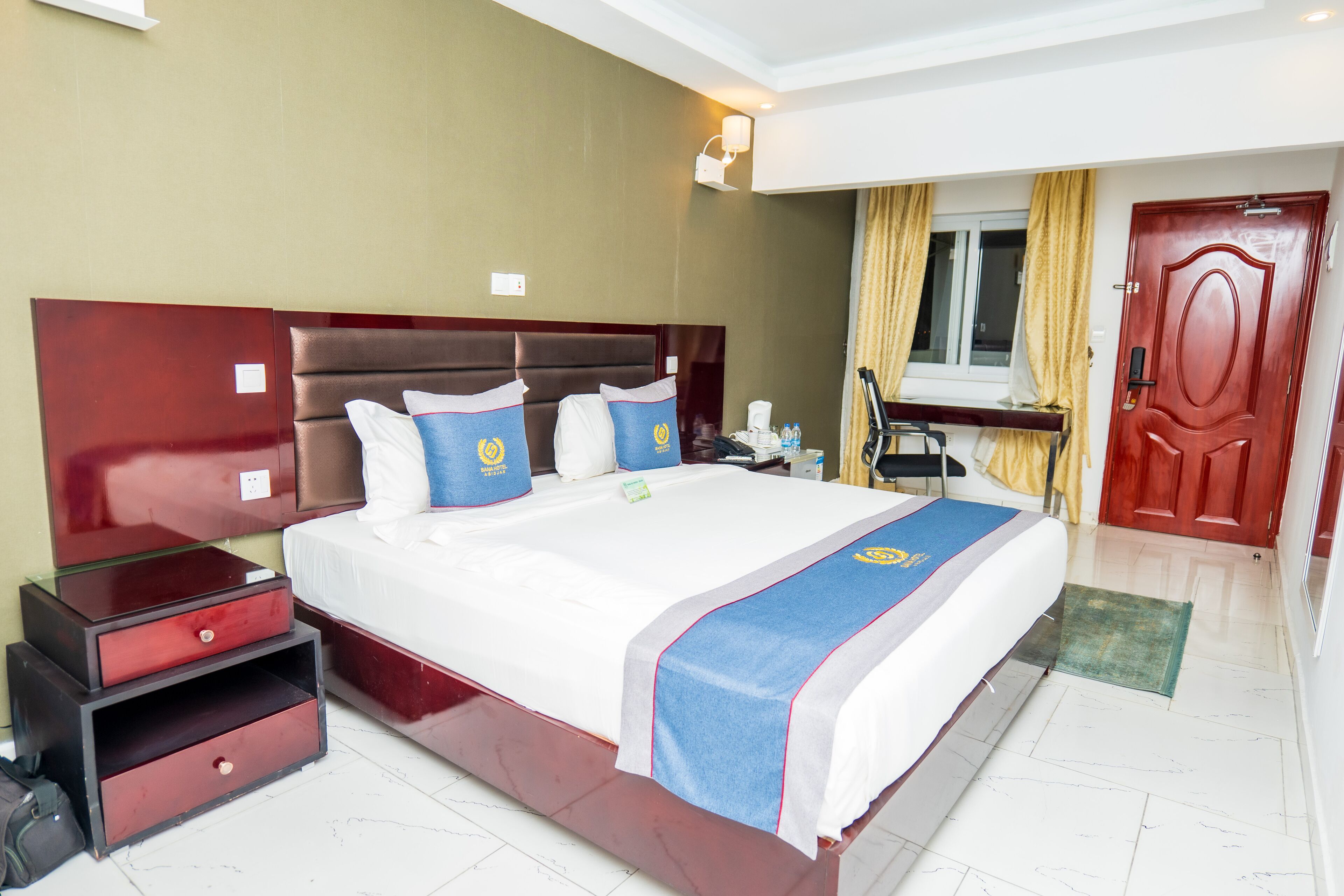Habitación de hotel con una cama grande, una mesita de noche, un escritorio con una silla y una puerta.