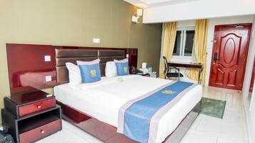 Habitación de hotel con una cama grande, una mesita de noche, un escritorio con una silla y una puerta.