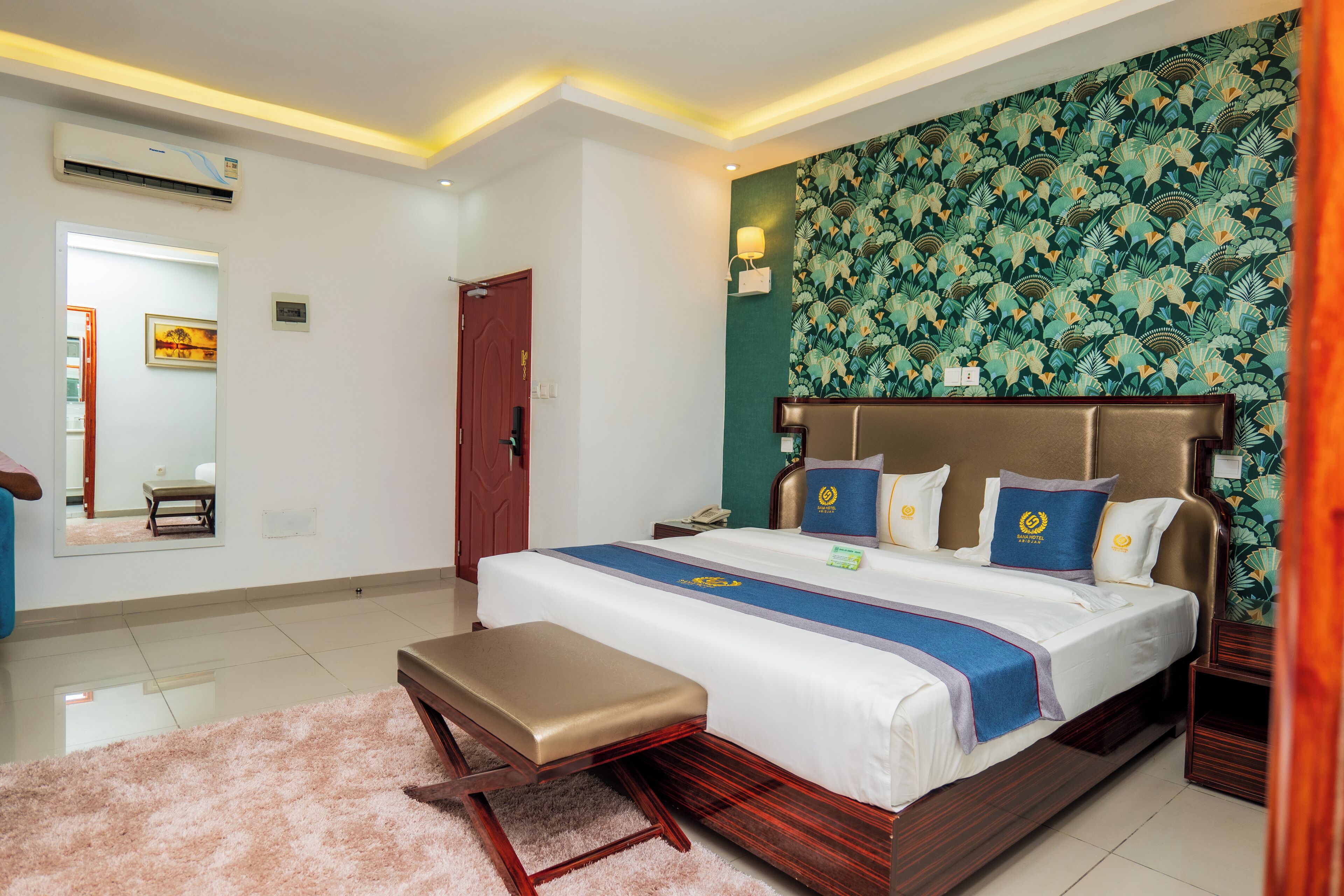 A hotel room with a large bed, a bench, a mirror, and a wall with a floral pattern.