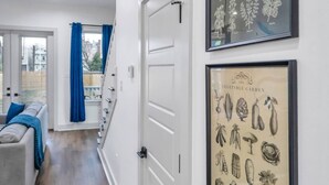 En hall med en vit dörr, en inramad botanisk illustration och en grå soffa med blå kuddar.