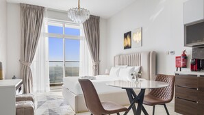 A modern hotel room with a large bed, a dining table with chairs, a chandelier, and a view of the city. - Premium Studio near Butterfly Garden w/ Pool & Gym (Dubai)