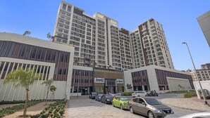 A modern building with multiple floors, a prominent 'Jewelz' sign, and a parking area with several cars. - Premium Studio near Butterfly Garden w/ Pool & Gym (Dubai)