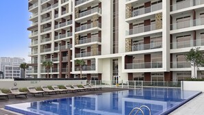 A modern hotel with a rooftop infinity pool, multiple balconies, and a clear sky. - Premium Studio near Butterfly Garden w/ Pool & Gym (Dubai)