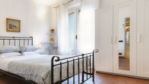 Een slaapkamer met een bed, een kledingkast, een nachtkastje, een lamp en een raam met gordijnen.
