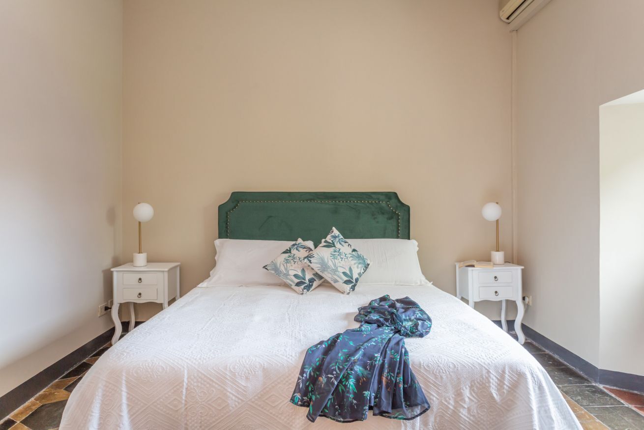Un lit bien fait, avec une tête de lit verte, deux tables de chevet avec des lampes et un plaid à motifs.