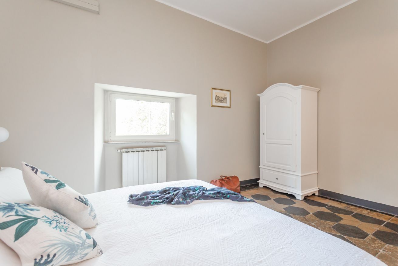 A bedroom with a bed, a window, a radiator, a wardrobe, and a picture on the wall.