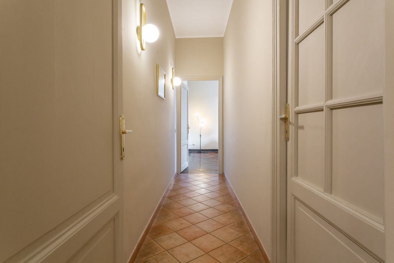 A hallway with white doors, a tiled floor, and wall-mounted light fixtures.