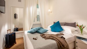 Une chambre d’hôtel avec un lit, une table de chevet avec une lampe, une valise et une fenêtre avec des rideaux.