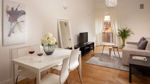 Un salon moderne avec une table à manger blanche, des chaises blanches, un meuble de télévision noir, un canapé beige et une plante en pot.