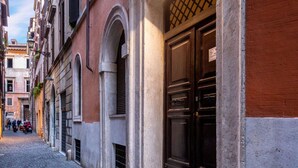 Une ruelle étroite pavée, bordée de bâtiments historiques dotés d’arcs en plein cintre et d’une porte en bois sombre particulièrement imposante.