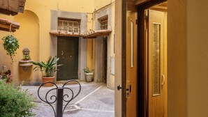 A narrow courtyard with a closed door, potted plants, and a metal gate. - Daplace - Mirta Apartment (Roma)