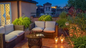 A rooftop terrace with a sofa, a round table with a book and glasses, and candles. - Daplace - Mirta Apartment (Roma)