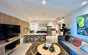 A modern living room with a flat-screen TV, a dining area with a table set for four, and a kitchen in the background. - Zenity Luxury Vacation Ho Chi Minh City (Ho Chi Minh City)