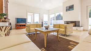 Un salon moderne avec un téléviseur à écran plat, deux canapés beige, une table basse en verre et une cheminée.