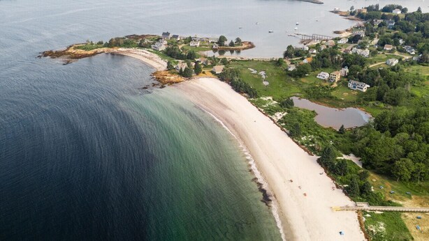 An aerial view of a coastal area with a sandy beach, a small settlement with houses, and a large body of water. - The Coastal Cottage | Walk to Pemaquid Beach | Fire Pit & Family-Friendly Retreat (Bristol)